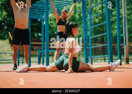 Donna che fa lo split stretch completo all'allenamento calistenico all'aperto con altri in sottofondo Foto Stock