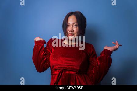 Giovane donna sicura di sé che stringe le mani alzate su uno sfondo blu da studio. Foto Stock