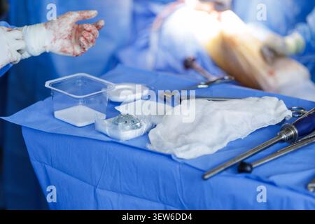 Una vista ravvicinata degli strumenti chirurgici e un'endoprotesi su un telo chirurgico blu durante un'operazione di sostituzione dell'anca, che mostra la precisione di Moder Foto Stock