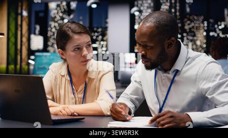 Scena dell'ufficio con partner che lavorano di notte su progetti aziendali, utilizzando computer per documentare la ricerca e la business intelligence. Brainstorming di squadra per definire obiettivi a lungo termine. Foto Stock