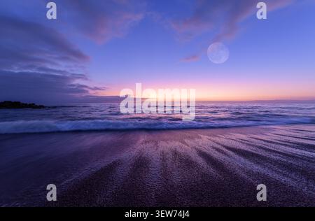 Una luna piena sorge su Una colorata scena dell'oceano al tramonto Foto Stock