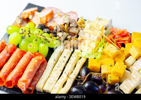Vassoio di formaggi disposto ad arte su una superficie di pietra scura. Uva fresca, salumi e formaggi assortiti creano un'elegante esposizione. Colori vivaci e morbidi Foto Stock