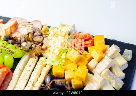 Vassoio di formaggi disposto ad arte su una superficie di pietra scura. Uva fresca, salumi e formaggi assortiti creano un'elegante esposizione. Colori vivaci e morbidi Foto Stock