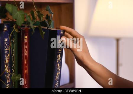 Mano che cerca un libro su una libreria di legno Foto Stock
