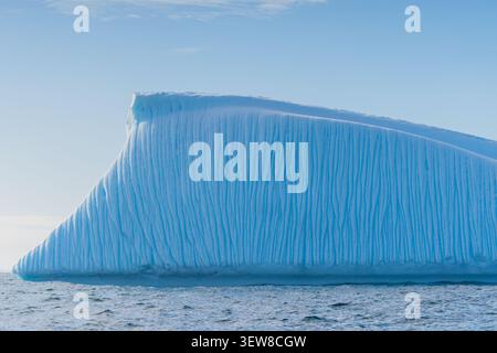 Primo piano di un enorme iceberg tabulare che galleggia nell'Oceano meridionale al largo della penisola Antartica, mostrando sorprendenti superfici di ghiaccio blu Foto Stock