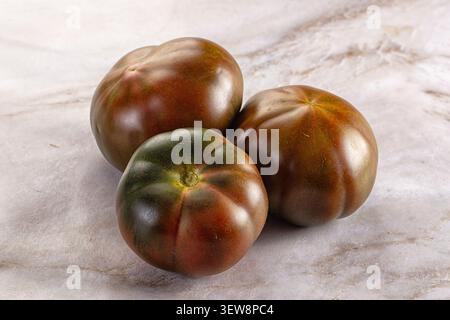 Tre pomodori maturi con sfumature verdi marroni, disposti su marmo chiaro. La luce naturale soffusa mette in risalto la pelle lucida con texture organica. Ideale Foto Stock