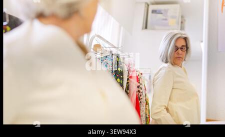 Donna matura che controlla i vestiti nello specchio da officina per cucire Foto Stock