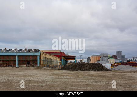 Cantiere con mucchi di terra e ghiaia di fronte ai vecchi edifici industriali in mattoni e allo skyline della città di Malmö in Svezia Foto Stock