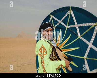 La gioiosa ballerina egiziana tanoura in un vivace costume verde porta la sua colorata gonna rotante color acqua davanti alle piramidi di Giza, ideale per il turismo culturale Foto Stock
