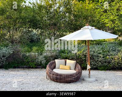 Un accogliente salotto all'aperto con un divano rotondo in vimini con cuscini Foto Stock