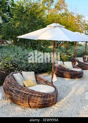 Un accogliente salotto all'aperto con un divano rotondo in vimini con cuscini Foto Stock