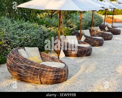 Un accogliente salotto all'aperto con un divano rotondo in vimini con cuscini Foto Stock