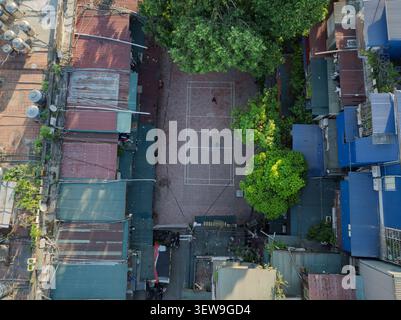 Droni sopra uno stretto cortile comune di Hanoi circondato da vecchi tetti di appartamenti, alberi e un piccolo campo sportivo dove le persone si riuniscono. Foto Stock