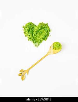 Forma a cuore verde in polvere di matcha organica e lussuoso cucchiaio dorato su sfondo bianco. Concetto di stile di vita sano e creativo. Un'idea di drink alla moda. Foto Stock