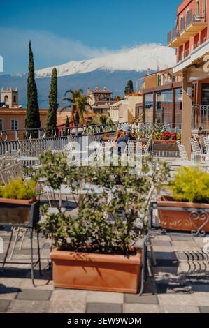Uomo che fuma di fronte all'Etna dalla soleggiata terrazza di Taormina Foto Stock