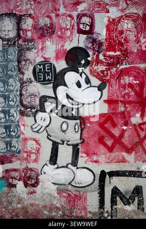 Primo piano di uno stencil di graffiti raffigurante un topolino dipinto su un muro della città intempestivo circondato da strati di Street art rossi e neri a Barcellona Foto Stock