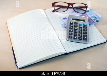 Quaderno con carta foderata vuota, bicchieri, banconote in euro e calcolatrice, concetto di pianificazione delle finanze personali in un libro di bilancio familiare, copia spa Foto Stock