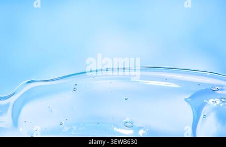 Onde macro con gel blu su un morbido sfondo pastello, bordo liquido lucido, composizione astratta minima, spazio di copia presente. Foto Stock