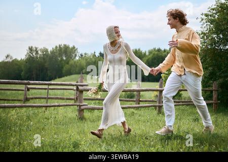 Gli amanti condividono un momento di gioia tenendosi per mano in un lussureggiante tramonto verde sotto il sole Foto Stock
