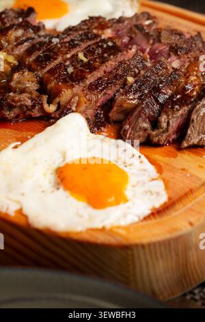 Bistecca di manzo medio-rara a fette con due uova fritte servita su un asse di legno. Foto Stock