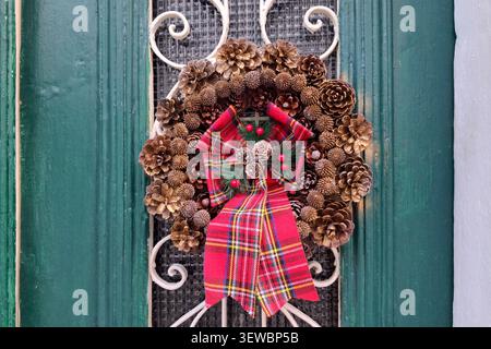 Corona di Natale in coni di pino con un grande nastro rosso, sulla porta d'ingresso di una casa. Foto Stock