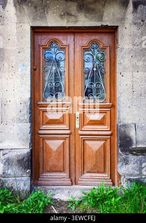 Vecchia porta doppia in legno con pannelli in vetro ornati. Porta inserita in un muro in pietra intemprata. Il muschio verde cresce alla base. Aspetto rustico e invecchiato con ricche tonalità di marrone Foto Stock