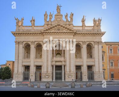 La maestosa facciata barocca tardo del'Arcibasilica di San Giovanni in Laterano sormontata da statue giganti sotto un cielo sereno a Roma, Italia Foto Stock