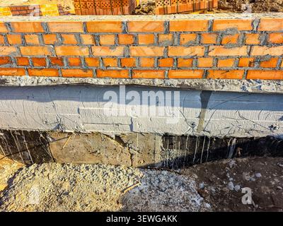 Vista ravvicinata di una fondazione dell'edificio in costruzione, caratterizzata da un muro in mattoni e strutture in cemento appena posate Foto Stock