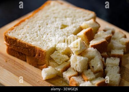 Pane bianco appena tagliato a cubetti su un tagliere di legno, pronto per preparare crostini fatti in casa, ripieni o pangrattato. Concetto di preparazione degli alimenti con testi Foto Stock