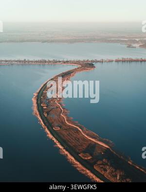 Vista aerea della stretta e curva striscia di terra di Scheendijk circondata da acque calme, con sponde erbose e una piccola strada a Scheendijk, Breukelen, U Foto Stock
