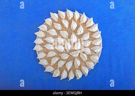 Foto ravvicinata ad alta risoluzione di gnocchi cinesi grezzi a forma di mezzaluna disposti ordinatamente su un tappeto di bambù rotondo, a fronte di una vivace linfa Foto Stock