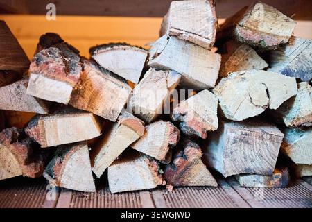 Pezzi di legna da ardere disposti in pile ordinate sotto la panca in legno nella sauna. Primo piano di tronchi asciutti per sistema di riscaldamento, interni termali caldi e concetto di comfort rustico Foto Stock