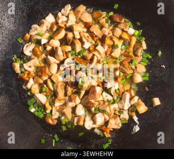 Funghi saltati a fette (boletus edulis, champignons e chanterelles) con cipolla, aglio e verdure in una ciotola nera. Vista ad angolo alto Foto Stock