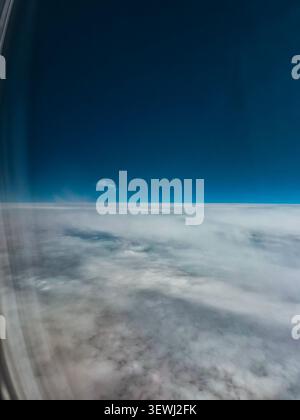 Strato nuvoloso e cielo blu visti attraverso la finestra dell'aereo in volo Foto Stock