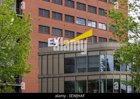 Eindhoven, Paesi Bassi - 13 giugno 2026: Il caratteristico logo EY Ernst & Young giallo e bianco in cima a un moderno edificio aziendale in mattoni surr Foto Stock