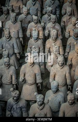 File di statue di guerrieri in terracotta a grandezza naturale, che variano in altezza e dettaglio, si stagliano in linee organizzate, mostrando sfumature di marrone, grigio e sott Foto Stock