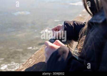 Primo piano di una donna che usa il gesso bianco per scrivere su una ringhiera in legno con sfondo ghiacciato durante il primo giorno di primavera. Foto Stock
