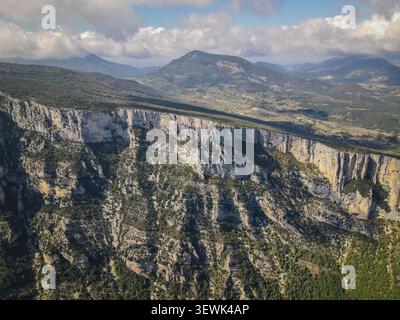 Un'ampia ripresa aerea cattura le spettacolari scogliere calcaree della Gola del Verdon, ricoperte da una vegetazione verde sparsa, con una valle profonda e un mou lontano Foto Stock