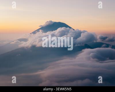Vista aerea della vetta del vulcano del Monte Batur che emerge da un mare denso di nuvole all'alba a Kintamani, Bali, Indonesia. Foto Stock