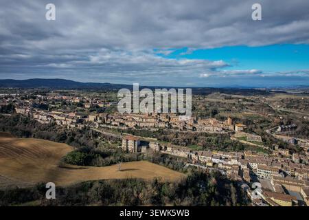Questa immagine aerea cattura una vista panoramica di una città storica densamente costruita annidata tra dolci colline e verdi campagne italiane. La scena fe Foto Stock