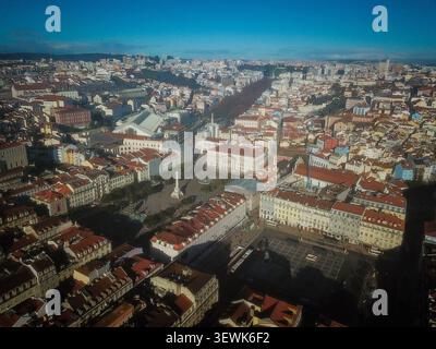 Una vista aerea a grandangolo cattura Piazza Rossio (Prac de D. Pedro IV) e il circostante quartiere Baixa Pombalina a Lisbona, Portogallo, con la città ro Foto Stock
