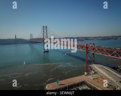 Un'ampia ripresa aerea cattura il ponte 25 de Abril che si estende attraverso il fiume Tago a Lisbona, in Portogallo, con la statua del Santuario del Cristo Re Foto Stock