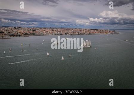 Un grandangolo aereo cattura il fiume Tago con una grande e storica barca a vela bianca e numerose barche a vela più piccole, sullo sfondo Foto Stock