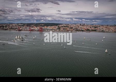 Un'ampia ripresa aerea cattura numerose barche a vela e un grande veliero che naviga sul fiume Tago, con la città di Lisbona visibile sullo sfondo un Foto Stock