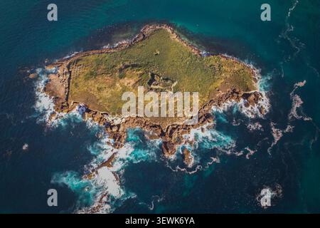 Uno scatto aereo cattura l'isola di Baleal vicino a Peniche, in Portogallo, circondata da acque turchesi e blu scuro dell'oceano con onde che si infrangono sulla sua roccia Foto Stock