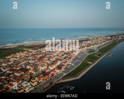 Un grandangolo aereo cattura la città di Costa Nova do Prado in Portogallo, mostrando i suoi caratteristici tetti con tegole rosse, una strada principale, spazi verdi, un Foto Stock