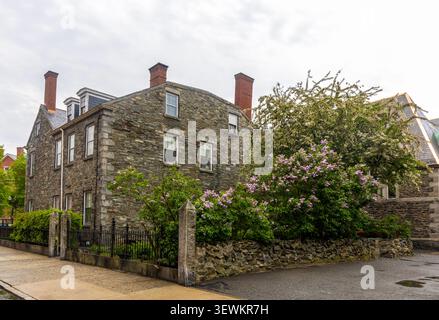 Splendida casa in pietra a Lowell, Massachusetts, con fiori viola in fiore nel suo giardino Foto Stock