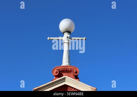 Lampada da strada vintage Heritage con lampada a globo bianca sulla parte superiore di un tetto architettonico decorato contro un cielo blu Foto Stock