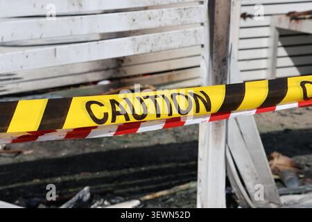Nastro di avvertenza giallo e nero che avvolge una struttura danneggiata con resti carbonizzati di un incendio Foto Stock