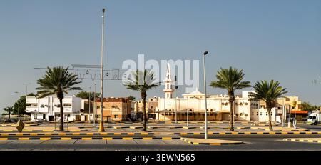 Vista panoramica degli edifici tradizionali e di una moschea nell'area storica di Yanbu in Arabia Saudita, caratterizzata da palme e un cielo azzurro. Foto Stock